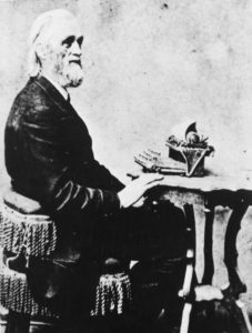 Portrait of Christopher Latham Sholes posing at a typewriter. (Courtesy of <a href=" https://www.wisconsinhistory.org/Records/Image/IM3218" target="_blank">Wisconsin Historical Society</a>)