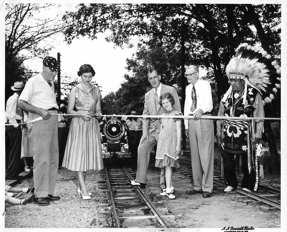 The Riverside & Great Northern Railway held a grand opening in Wisconsin Dells on August 9, 1953. From left to right: Elmer Sandley, Judith Johnston, Milwaukee Road general passenger agent R.F. Johnston, Carol Johnston, Grover Belton, and Chief Yellow Thunder of the Ho-Chunk Nation. (Photo by H.H. Bennett Studio)