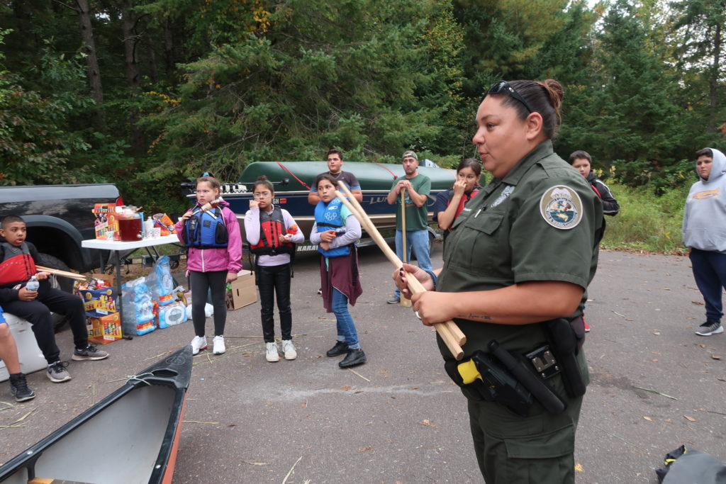 Christine Dzwonkowski, a warden with the Great Lakes Indian Fish and Wildlife Commission, gives Bad River youth a tutorial on how to harvest wild rice at Pacwawong Lake. (Danielle Kaeding/WPR)